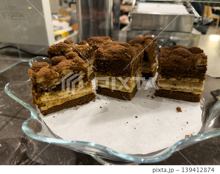 Delicious layered mini tiramisu cakes, richly dusted with cocoa powder, elegantly displayed on a glass dish for cafe dessert offerings Delicious layered mini tiramisu cakes, richly dusted with cocoa powder, elegantly displayed on a glass dish for cafe dessert offerings 139412874