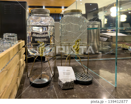 Two glass drink dispensers with water and sparkling water, offering self-service refreshment at a hotel buffet, promoting guest hydration and convenience 139412877