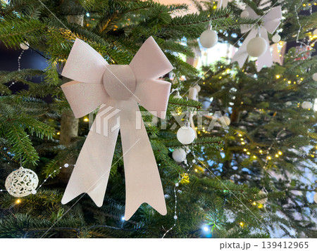 Elegant Christmas tree with a glittery pink bow, white ornaments, and warm lights, symbolizing festive holiday spirit and winter celebration 139412965