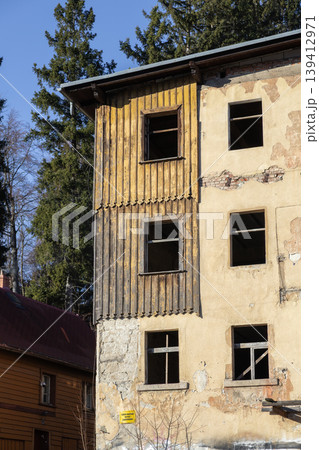 Abandoned multi-story building facade with weathered wooden planks, broken windows, peeling plaster, symbolizing urban decay and renewal 139412971
