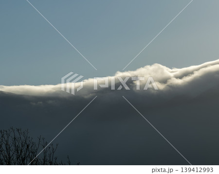 Sunlit horizontal cloud layer creates dramatic contrast above dark, stormy weather under clear sky, showcasing nature's powerful atmospheric changes 139412993