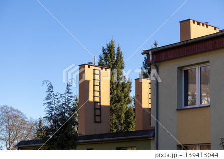 Tall yellow building structures with ladders and lush green trees against a clear blue sky, highlighting modern urban architecture on a bright day Tall yellow building structures with ladders and lush green trees against a clear blue sky, highlighting modern urban architecture on a bright day 139413044
