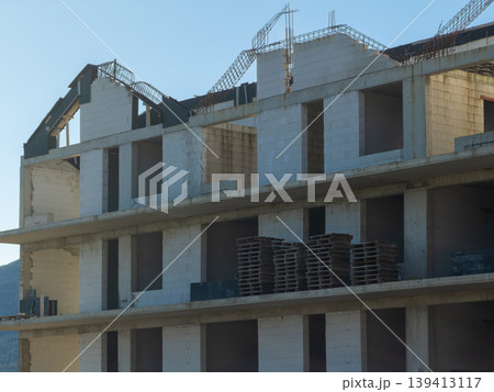 An unfinished concrete residential building is under construction with exposed brick walls and wooden pallets on the floor, representing architectural development, urban growth, and housing projects 139413117