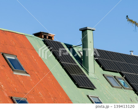 Solar panels are installed on a vibrant green and orange corrugated metal residential roof to promote sustainable energy solutions, renewable power generation, and modern eco-friendly living today 139413120