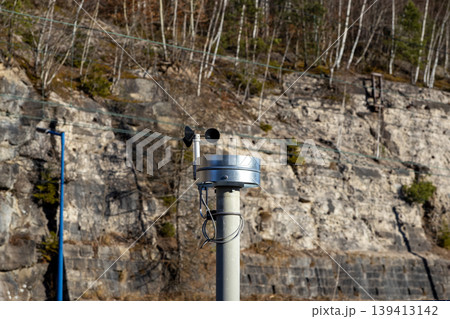 Anemometer measuring wind speed and direction on a metal post, set against a rocky mountain slope to emphasize meteorological monitoring, environmental research, and weather data collection technology 139413142