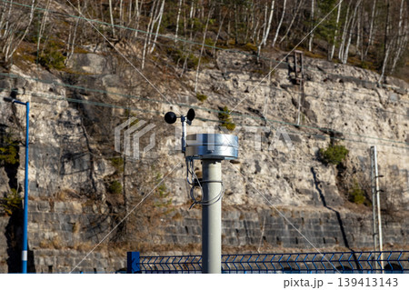 An anemometer measuring wind speed is mounted on a pole against a rocky cliff, representing environmental monitoring, meteorological research, climate data collection, and atmospheric study technology An anemometer measuring wind speed is mounted on a pole against a rocky cliff, representing environmental monitoring, meteorological research, climate data collection, and atmospheric study technology 139413143