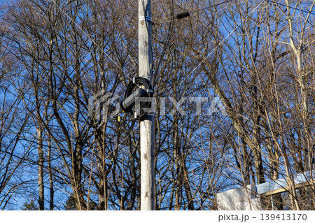 A fiber optic splice closure is mounted on a wooden utility pole with black communication cables, representing modern telecommunications infrastructure and global internet connectivity in a suburbia A fiber optic splice closure is mounted on a wooden utility pole with black communication cables, representing modern telecommunications infrastructure and global internet connectivity in a suburbia 139413170