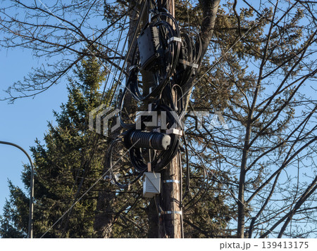 A fiber optic cable distribution box is securely mounted on a tall wooden utility pole, showcasing essential network infrastructure and modern telecommunications connectivity under a bright blue sky A fiber optic cable distribution box is securely mounted on a tall wooden utility pole, showcasing essential network infrastructure and modern telecommunications connectivity under a bright blue sky 139413175