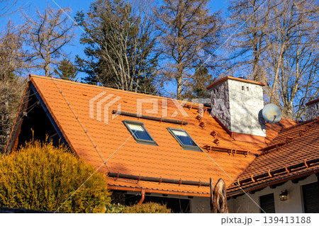 Orange tile roof with skylights and stone chimney on a rural house exterior, representing residential architecture, autumn season, warmth, cozy living, building maintenance and real estate concepts Orange tile roof with skylights and stone chimney on a rural house exterior, representing residential architecture, autumn season, warmth, cozy living, building maintenance and real estate concepts 139413188
