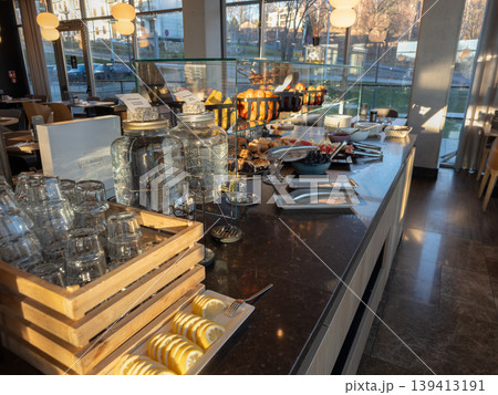 Breakfast buffet counter with fresh fruit and water dispensers in a bright hotel dining room, highlighting hospitality services, morning catering, healthy nutrition, and restaurant interior design Breakfast buffet counter with fresh fruit and water dispensers in a bright hotel dining room, highlighting hospitality services, morning catering, healthy nutrition, and restaurant interior design 139413191