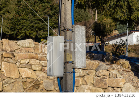 An electrical distribution box and fiber optic terminal are mounted on a concrete utility pole to provide essential power grid connection and high speed internet connectivity in a residential suburb 139413210