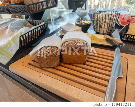 Fresh whole grain loaves with sunflower seeds served on a wooden cutting board with a knife at a hotel breakfast buffet, representing healthy morning meal options, hospitality, and catering services 139413211