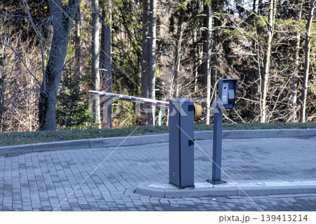 An automated security boom barrier at a residential delivery zone entrance manages vehicular traffic and access control within a forest environment to ensure property safety and organized logistics 139413214