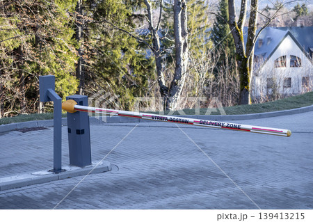 An automated security boom barrier arm with Delivery Zone text controls vehicle access to a restricted private property, logistics site, or professional loading area for efficient transport management 139413215