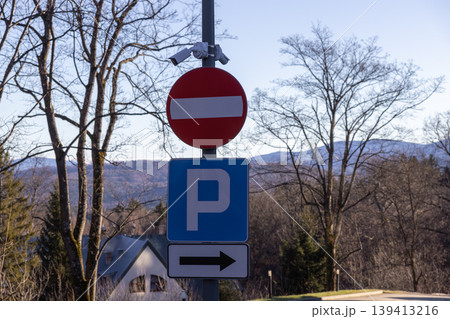 Road signs indicating no entry and parking lot direction mounted on a metal pole with surveillance cameras, emphasizing traffic regulation, urban navigation, and security monitoring in a quiet area Road signs indicating no entry and parking lot direction mounted on a metal pole with surveillance cameras, emphasizing traffic regulation, urban navigation, and security monitoring in a quiet area 139413216