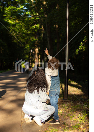 Curious boy and his mom stand under tree, gazing up with awe at birds nest. This image embodies innocence and the simple childhood joy of exploring outdoors Curious boy and his mom stand under tree, gazing up with awe at birds nest. This image embodies innocence and the simple childhood joy of exploring outdoors 139413231