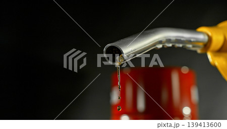 Gasoline drops dripping from fuel nozzle on dark background, minimal fuel flow. Concept of fuel depletion, shortage and energy crisis, macro detail, dramatic lighting. 139413600