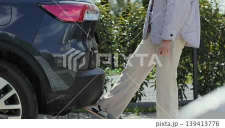Old woman opens the trunk and takes out a bag. Automatic system opening the trunk by leg. Old woman opens the trunk and takes out a bag. Automatic system opening the trunk by leg. 139413776