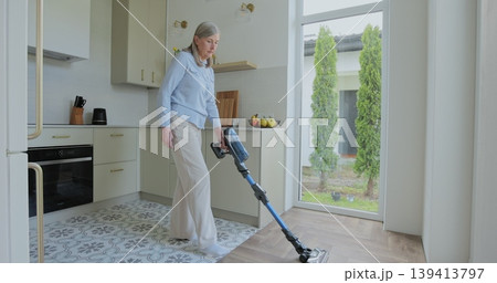 Wireless vacuum machine and senior woman cleaning floor in kitchen at home apartment. Wireless vacuum machine and senior woman cleaning floor in kitchen at home apartment. 139413797