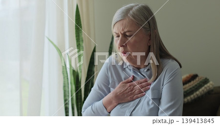 Senior woman, chest inflammation and cardiovascular emergency in lounge, panic attack and physical symptoms. Senior woman, chest inflammation and cardiovascular emergency in lounge, panic attack and physical symptoms. 139413845