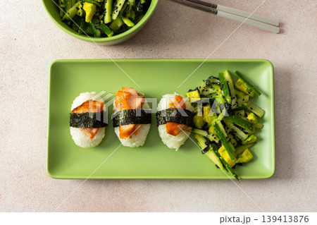 Food is arranged on a green plate with salad made of nori, cucumbers, and avocado alongside nagiri sushi topped with red fish, suitable for breakfast or lunch Food is arranged on a green plate with salad made of nori, cucumbers, and avocado alongside nagiri sushi topped with red fish, suitable for breakfast or lunch 139413876