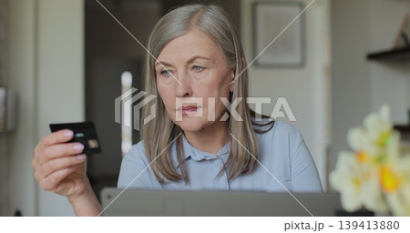 Old woman senior granny with laptop and bank credit card paying online shopping with computer buying internet payment. Online purchase. 139413880