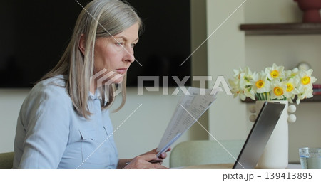 Senior woman working with laptop while checking some documents at home. Remote work concept. 139413895