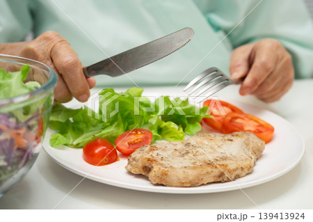 Asian elderly woman patient eating pork chop stake and vegetable salad for healthy food in hospital. Asian elderly woman patient eating pork chop stake and vegetable salad for healthy food in hospital. 139413924