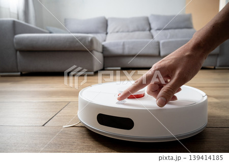 Hand pressing button on robot vacuum cleaner in modern home Hand pressing button on robot vacuum cleaner in modern home 139414185