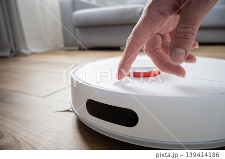 Hand pressing button on robot vacuum cleaner in modern home 139414186