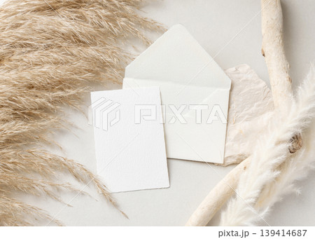 Card and envelope mockup on beige stone with driftwood and pampas grass, wedding stationery 139414687