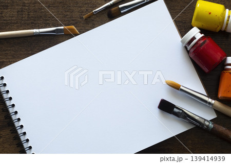 Sketchbook with paint brushes and paint tubes on wooden table with copy space, top view 139414939