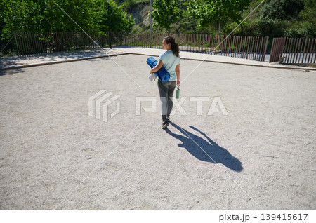 Woman Carrying Yoga Mat and Water Bottle Walking Outdoors in Sunny Park Woman Carrying Yoga Mat and Water Bottle Walking Outdoors in Sunny Park 139415617