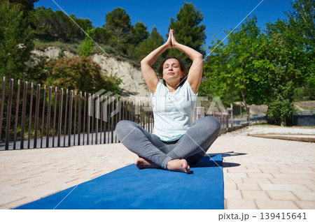 Woman Practicing Outdoor Yoga Meditation On Mat In Sunny Park For Wellness And Fitness 139415641