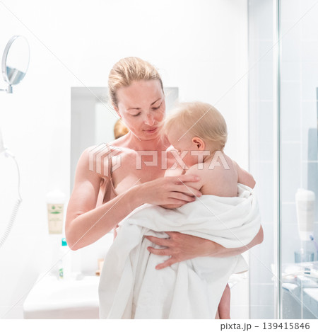 Tender mother holding her baby boy wrapped in a white towel after a bath. Loving connection between a mother and her child in a peaceful moment at home. Tender mother holding her baby boy wrapped in a white towel after a bath. Loving connection between a mother and her child in a peaceful moment at home. 139415846