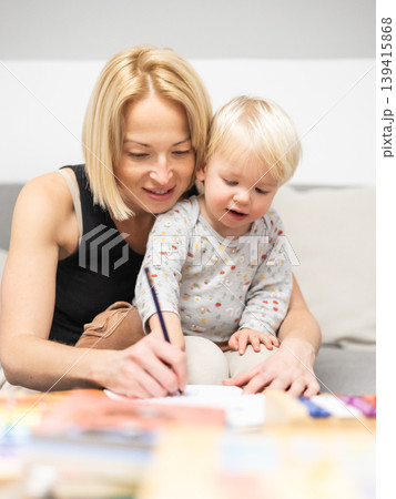 Caring young Caucasian mother and small son drawing painting in notebook at home together. Loving mom or nanny having fun learning and playing with her little 1,5 year old infant baby boy child Caring young Caucasian mother and small son drawing painting in notebook at home together. Loving mom or nanny having fun learning and playing with her little 1,5 year old infant baby boy child 139415868