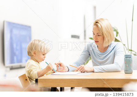 Caring young Caucasian mother and small son drawing painting in notebook at home together. Loving mom or nanny having fun learning and playing with her little 1,5 year old infant baby boy child Caring young Caucasian mother and small son drawing painting in notebook at home together. Loving mom or nanny having fun learning and playing with her little 1,5 year old infant baby boy child 139415873