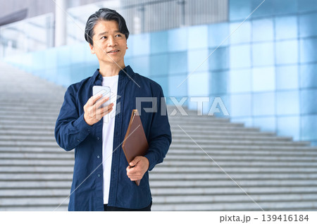 屋外でスマートフォンを持ち遠くを見る50代日本人男性 139416184