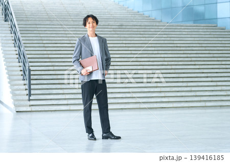 赤茶のファイルを抱え屋外の階段前に立つ30代日本人男性 139416185