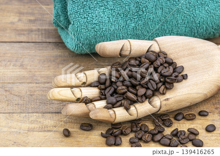 Articulated Wooden Hand Holding Fresh Roasted Coffee Beans Used to Exfoliate Skin in Natural Spa Beauty Treatment on Rustic Wood Articulated Wooden Hand Holding Fresh Roasted Coffee Beans Used to Exfoliate Skin in Natural Spa Beauty Treatment on Rustic Wood 139416265