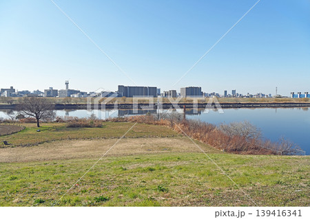 河川敷に広がる開放的な風景 澄み渡る青空と穏やかな水面に映る都会のビル群が織りなす静寂 河川敷に広がる開放的な風景 澄み渡る青空と穏やかな水面に映る都会のビル群が織りなす静寂 139416341