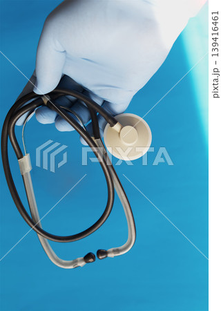 A hand wearing a blue medical glove holding a stethoscope against a blue background, symbolizing professional emergency care and healthcare. A hand wearing a blue medical glove holding a stethoscope against a blue background, symbolizing professional emergency care and healthcare. 139416461
