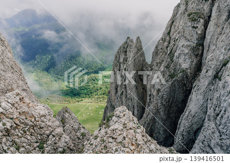 Rocky cliffs above green valley with mist and clouds in mountain landscape Rocky cliffs above green valley with mist and clouds in mountain landscape 139416501