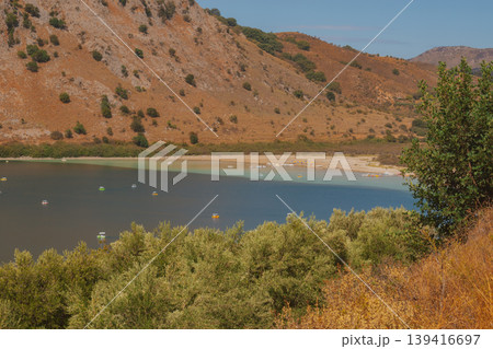 Drying mountain lake with wide strip of dried shore and orange rocky slope. Drying mountain lake with wide strip of dried shore and orange rocky slope. 139416697