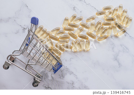 A creative shot of a miniature shopping cart overflowing with golden Omega-3 capsules on a white marble background. Perfect for health e-commerce and wellness marketing A creative shot of a miniature shopping cart overflowing with golden Omega-3 capsules on a white marble background. Perfect for health e-commerce and wellness marketing 139416745