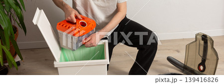 A 53-year-old man is getting ready to clean the floor with a vacuum cleaner. He is kneeling in a room that has plants and a bed nearby. The area looks tidy and organized, banner A 53-year-old man is getting ready to clean the floor with a vacuum cleaner. He is kneeling in a room that has plants and a bed nearby. The area looks tidy and organized, banner 139416826