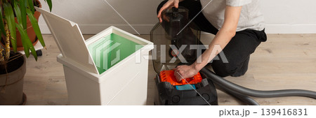 A 53-year-old man is getting ready to clean the floor with a vacuum cleaner. He is kneeling in a room that has plants and a bed nearby. The area looks tidy and organized, banner A 53-year-old man is getting ready to clean the floor with a vacuum cleaner. He is kneeling in a room that has plants and a bed nearby. The area looks tidy and organized, banner 139416831