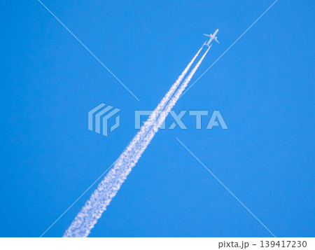 Airplane flying high in the sky leaving white trails during clear day with blue background Airplane flying high in the sky leaving white trails during clear day with blue background 139417230