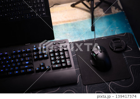 Modern dark gaming keyboard and mouse setup with laptop on desk, illuminated for computing Modern dark gaming keyboard and mouse setup with laptop on desk, illuminated for computing 139417374