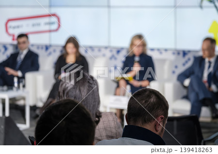 Business conference panel discussion with audience in foreground, speakers on stage during corporate event Business conference panel discussion with audience in foreground, speakers on stage during corporate event 139418263